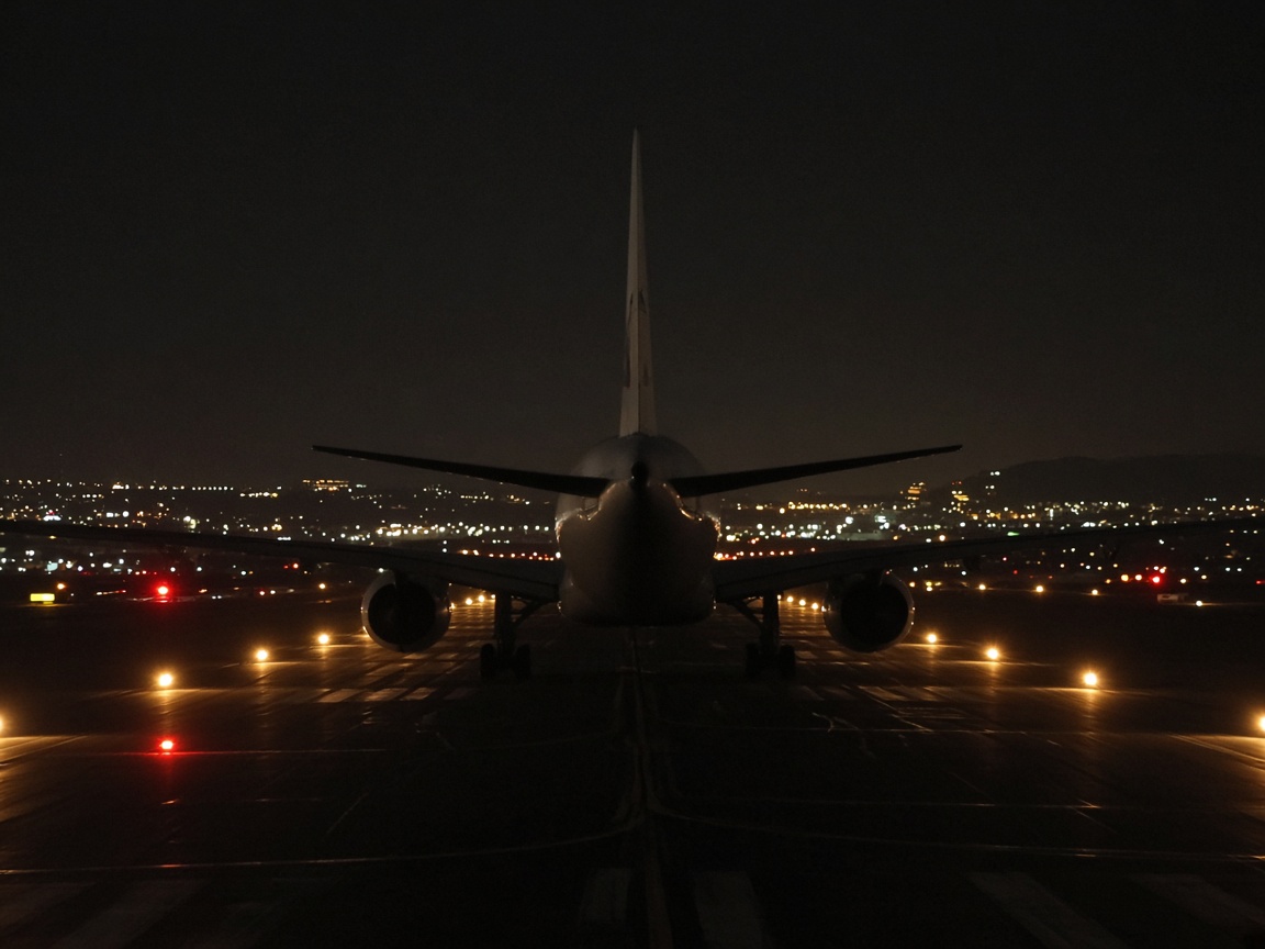 Avion de dos sur une piste, la nuit, avec les lumières de la ville